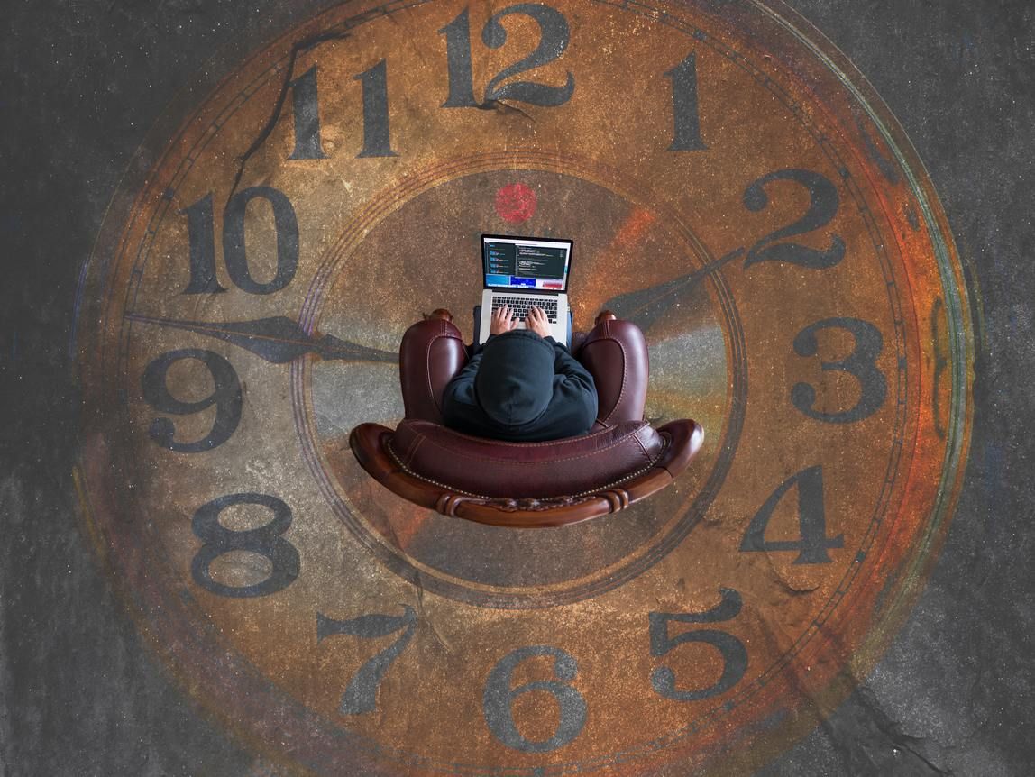 A freelancer types furiously on a computer trying to meet a deadline, while surrounded by a ticking clock.