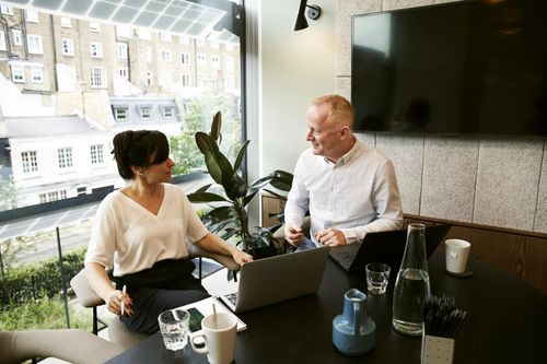 A freelance consultant and a client sit in an office at a desk discussing digital marketing