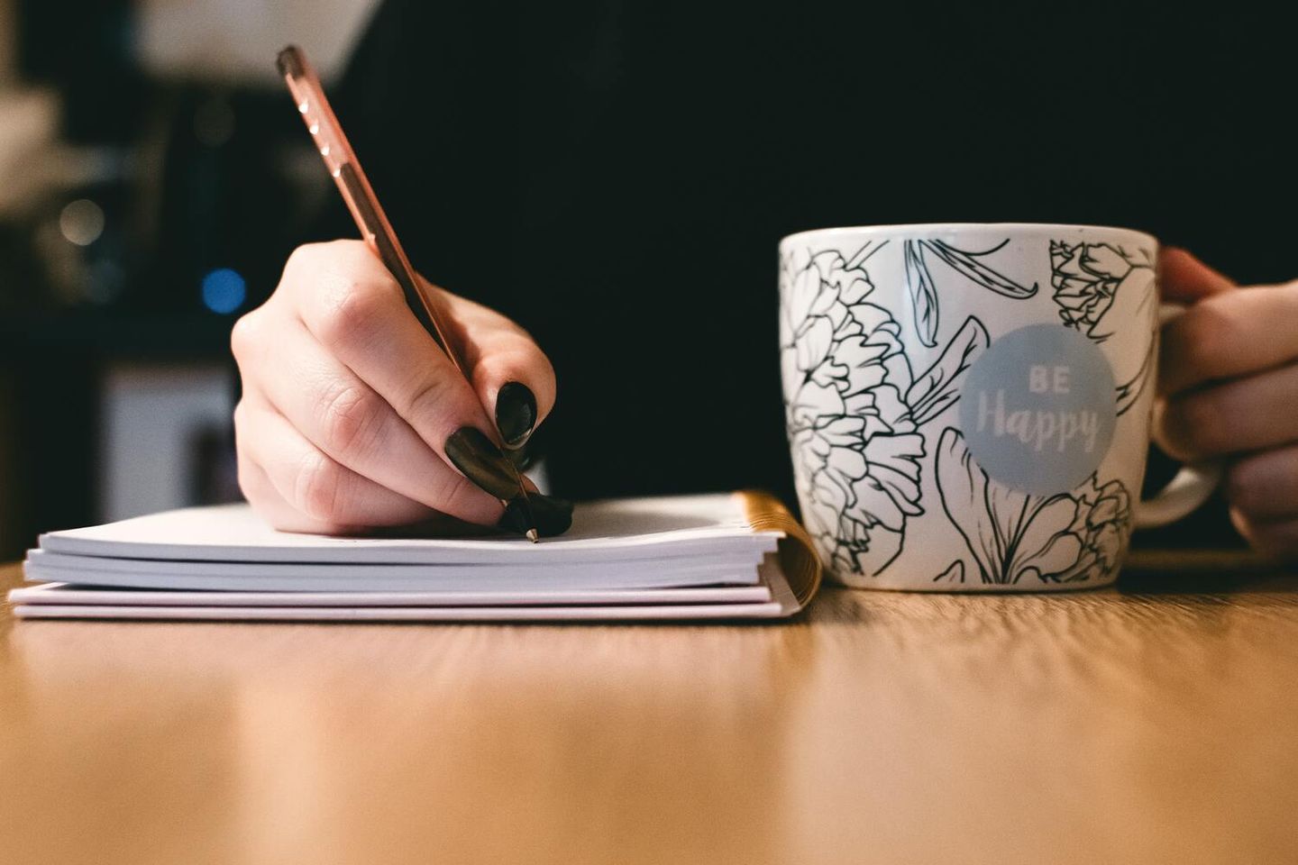 Freelance writer sitting at a desk, writing in a notebook while drinking from a mug
