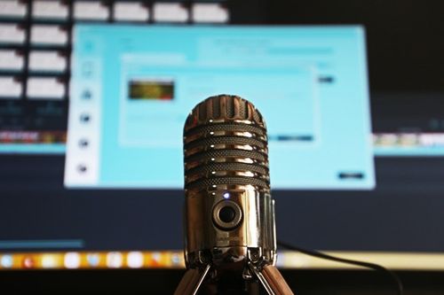 Close-up of a recording microphone with computer and recording software in the background