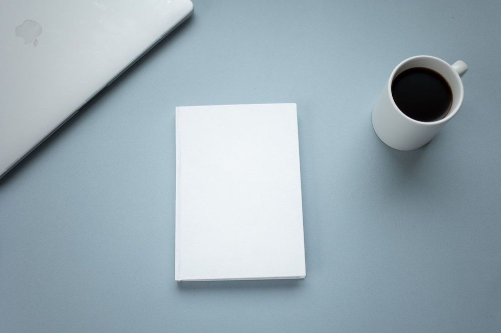 A cup of coffee is on the table with the laptop and notebook