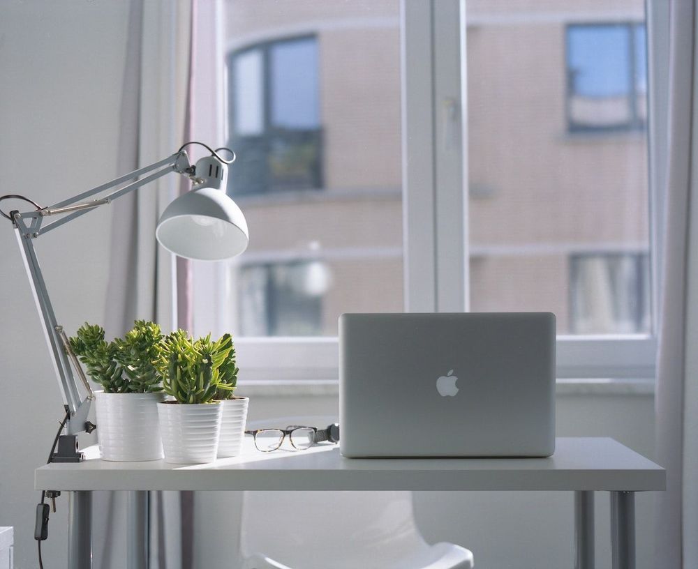 Laptop and desk lamp are on the table near the window