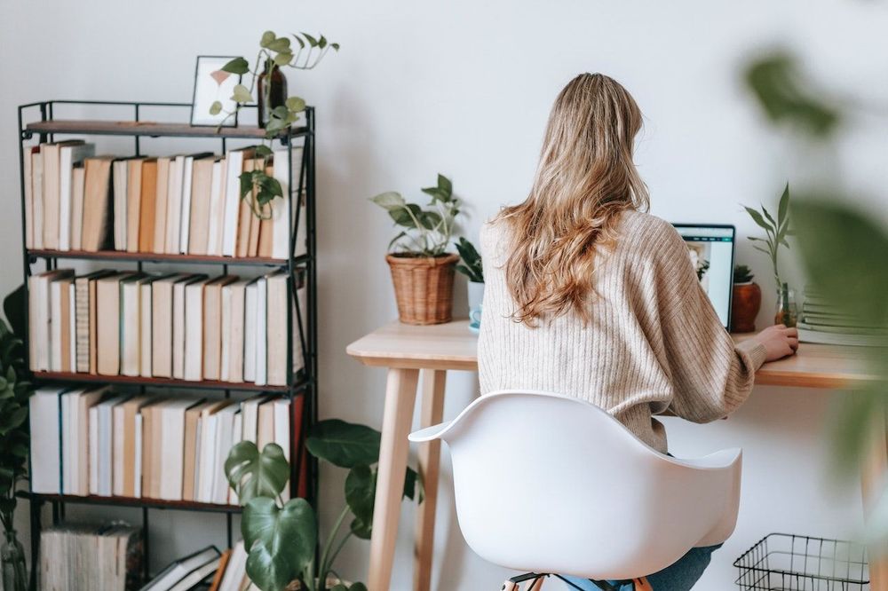 Freelancer is working at her home office with a small library in it