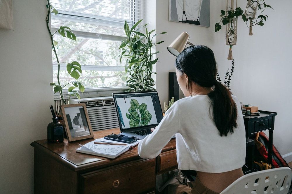 Freelancer is working in front of the window at her home office with the plants