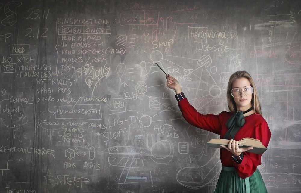 The freelance teacher is standing near the blackboard 