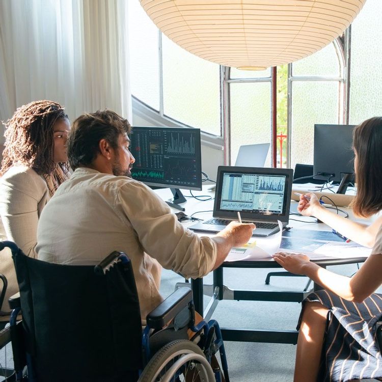 Man in a wheelchair at a computer working with two female coworkers