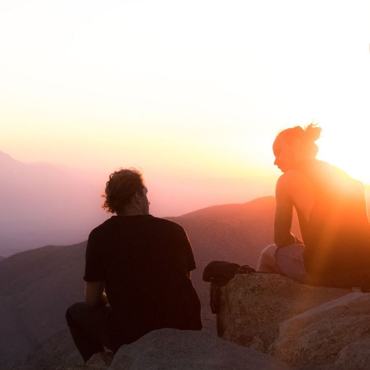 Two men sit on a rock at sunset in the mountains