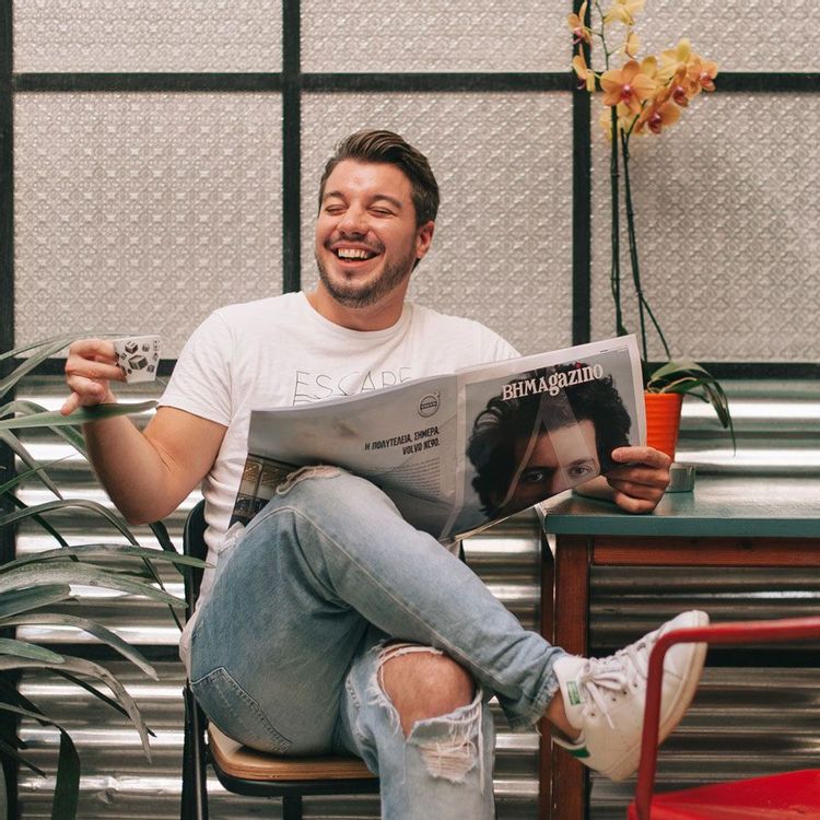 Man holding small mug and reading a newspaper while smiling.