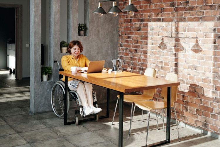 A woman in a wheelchair sips coffee in front of her laptop in an office